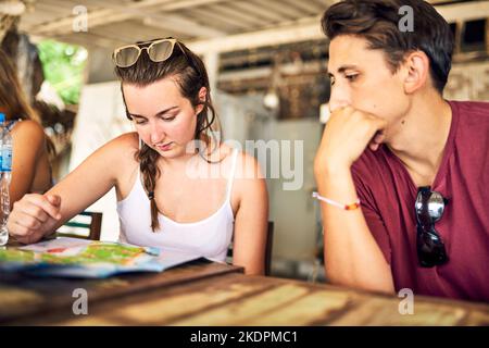 Was denken Sie darüber nach? Zwei junge Freunde schauen sich gemeinsam ein Menü an, während sie sich in einem Restaurant entspannen. Stockfoto