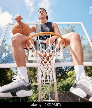 Sport, Basketball und Mann, der auf einem Basketballkorb sitzt und sich auf das Training, Match oder Wettkampf im Freien auf dem Basketballplatz vorbereitet. Hochformat Stockfoto