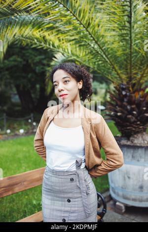 Junge afroamerikanische multirassische Frau in brauner Jacke im Park oder auf der Straße im Freien. Herbst- oder Frühjahrssaison Stockfoto