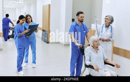 Patientenversorgung im Krankenhaus. Freundliches medizinisches Personal kümmert sich um die Gesundheit der älteren Frau, die auf einem medizinischen Rollstuhl im Flur der medizinischen Einrichtung sitzt Stockfoto