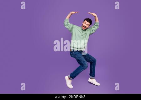 In voller Länge Foto von schönen jungen Mann halten fallen schweren leeren Raum tragen trendige grau isoliert auf violetten Hintergrund Stockfoto