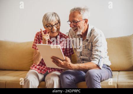 Ältere Paare sitzen im Wohnzimmer und plaudern mit ihrer Familie auf einem digitalen Tablet. Stockfoto