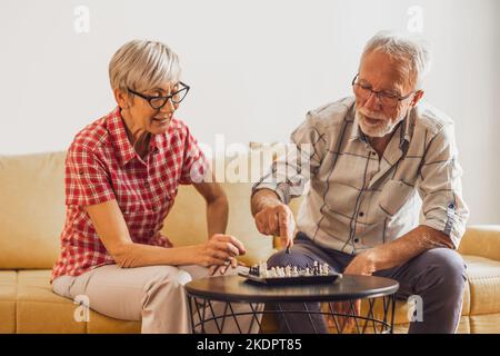 Seniorenpaar sitzt im Wohnzimmer und spielt Schach. Freizeitaktivitäten. Stockfoto