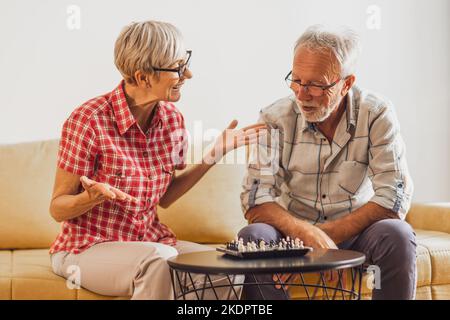 Seniorenpaar sitzt im Wohnzimmer und spielt Schach. Freizeitaktivitäten. Stockfoto
