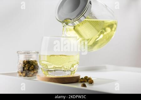 Gießt auf dem weißen Tisch Chrysantheme heißen Tee ins Glas Stockfoto