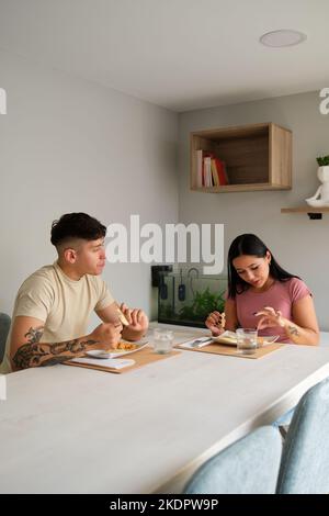 Zwei junge lateinische Menschen essen traditionelle Arepas im Wohnzimmer. Stockfoto