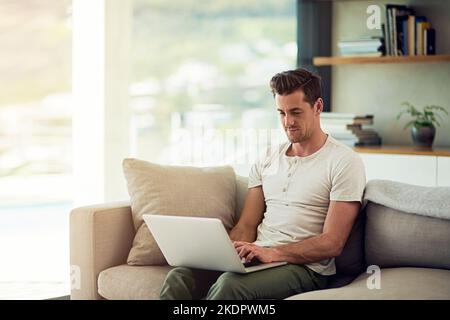 Ein junger Mann, der zu Hause einen Laptop auf dem Sofa benutzt. Stockfoto