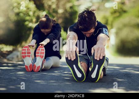 Durch ihre Aufwärmroutine gehen. Ganzkörperaufnahme von zwei jungen Menschen, die sich vor dem Training im Freien aufwärmen. Stockfoto