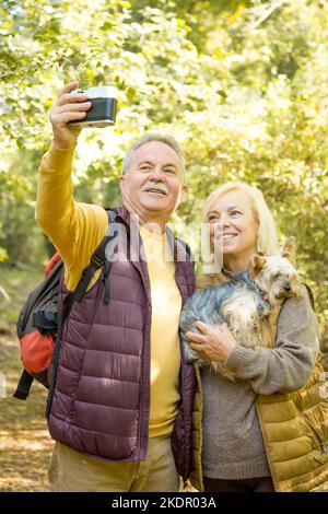Vertikales Foto eines reifen Paares mit einem Yorkshire-Hund und einem Selfie im Wald Stockfoto