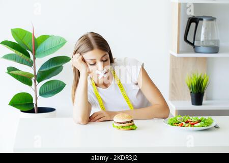 Frau mit aufgeklebtem Mund sitzt an einem Tisch mit Fast Food. Stockfoto