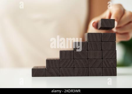 Frau legte und stapelte leere Holzwürfel mit der Hand auf den Schreibtisch Stockfoto