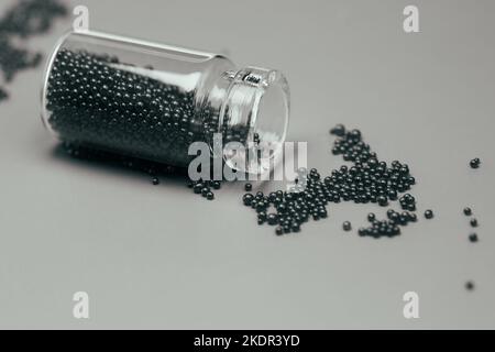 Schwarze Farbe glitzert in einer kleinen Glasflasche isoliert auf grauem Hintergrund Seitenansicht Kopierraum. Wunderschöne Schwarz-Weiß-Stillleben-Fotografie. Stockfoto