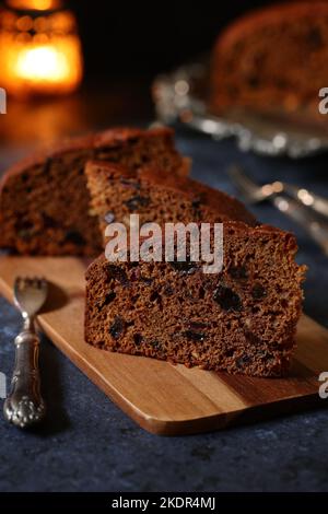 Scheiben von traditionellem, hausgemachtem, reichem Obst und Guinness-Stout-Kuchen auf einer dekorativen Silberplatte mit dekorativen Dessertgabeln und Kerzenlicht Stockfoto