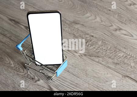 Smartphone mit leerem weißen Bildschirm im Einkaufswagen mit Kopierplatz. Mobiles Shopping-Konzept Stockfoto