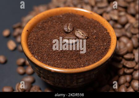 Eine Tasse Kaffee mit Bohnen in der Nähe verstreut, drei Kaffeebohnen liegen auf gemahlenem Kaffee. Stockfoto