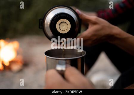 Ein paar Reisende trinken Kaffee. Mann gießt Tee aus Thermoskannen. Picknick am Strand. Frau hält Metallbecher mit Getränk. Lifestyle Moment in der Natur Stockfoto