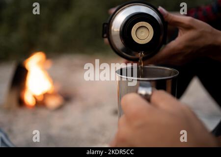 Aus einer Thermoskanne gießen. Frau gießt Kaffee in eine Tasse für den Mann. Tourismus- und Reisekonzept. Herbstfotos. Stockfoto