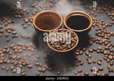 Kaffeetassen und geröstete Kaffeebohnen auf schwarzem Hintergrund in einem Paar, schwarze Kaffeebohnen, gemahlen und frisch gebrüht. Stockfoto