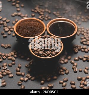 Tassen Kaffee unter ausgewählten und kalibrierten Arabica-Kaffeebohnen, verteilt auf schwarzem Hintergrund, drei aromatische Tassen Kaffee in einem Paar. Stockfoto