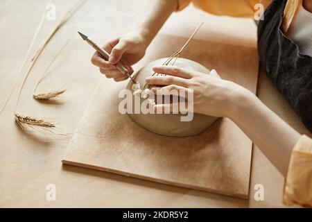 Draufsicht Nahaufnahme der weiblichen Kunsthandwerkerin, die handgemachte Keramik mit Pflanzenabdruck unter Verwendung von immorteller Blume, Kopierraum schmückt Stockfoto