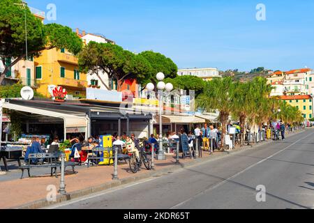 SANREMO, ITALIEN - 28. OKTOBER 2021: Menschen essen in Restaurants Straßenterrassen bei strahlendem Sonnenschein, Stadtbild mit grünen Bäumen Stockfoto