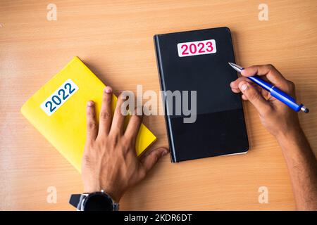 Draufsicht auf die Hände, die 2022 alte Tagebuch durch eine neue Molkerei für das neue Jahr 2023 ersetzen Stockfoto