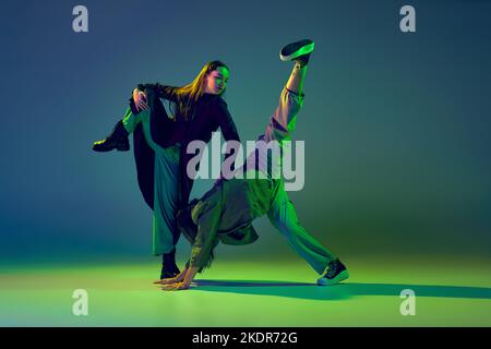 Zwei Tänzerinnen, ein stilvolles, modisches Tanzpaar, tanzen auf farbenprächtiger blau-grüner Hintergrundfarbe in Neonlicht zeitgenössischen Tanz. Konzept der Kunst Stockfoto