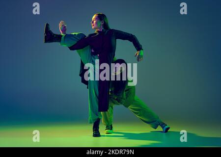 Zwei Tänzerinnen, ein stilvolles, modisches Tanzpaar, tanzen auf farbenprächtiger blau-grüner Hintergrundfarbe in Neonlicht zeitgenössischen Tanz. Konzept der Kunst Stockfoto