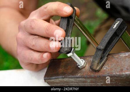 Eine Männerhand schraubt einen Bolzen in eine Metallmutter. Arbeiten mit Metall Stockfoto