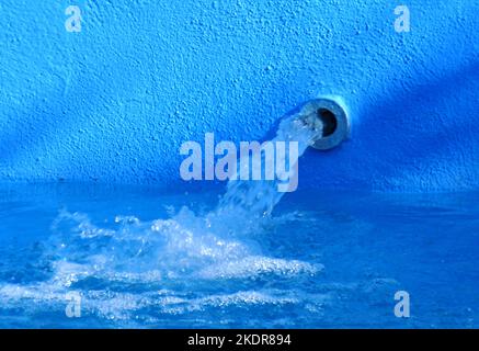 Wasserstrahl, der aus einem Auslauf in einem Swimmingpool mit blau gestrichenen Wänden austritt Stockfoto