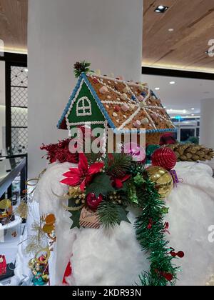 Schönes Lebkuchenhaus auf Baumwollschnee und andere Weihnachtsdekorationen platziert. Stockfoto