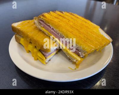 Gegrilltes Schinken- und Käsesandwich, serviert auf einem weißen Teller und auf einem dunkelbraunen Holztisch. Stockfoto
