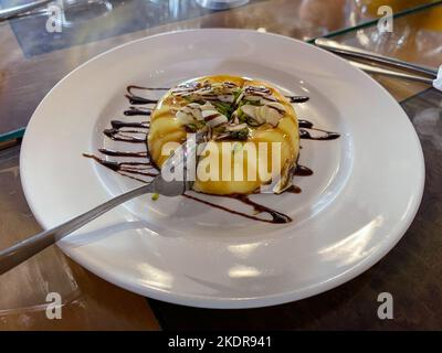 Karamellpudding serviert auf einem weißen Teller mit geschnittenen Mandeln und Pistazien. Stockfoto