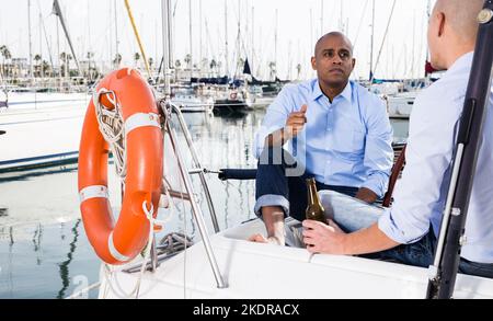 Ein paar Jungs in blauen Hemden und Jeans plaudern auf einer privaten Yacht im Hafen Stockfoto