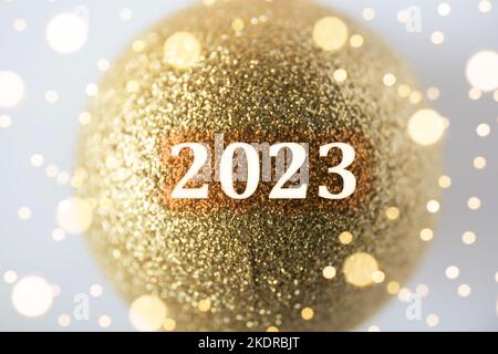 Frohes neues Jahr! Konzept für das neue Jahr 2023. Jahreszahl auf goldener Glitzer-Weihnachtskugel. Innenaufnahmen, Studioaufnahmen. Stockfoto