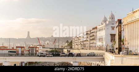 Gebäude der Volksversammlung und des Hauptquartiers von Wilaya mit fliegenden Vögeln, geparkten Autos und arabischen Flaggen und dem Denkmal des Märtyrers. Stockfoto