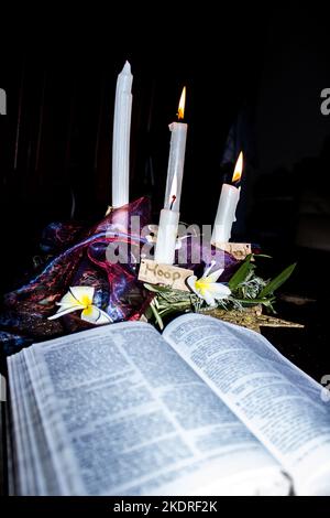 Moderner Kranz aus vier Adventskerzen mit einer offenen Bibel im Vordergrund. Stockfoto