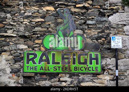 Altes emailliertes Werbeschild für Raleigh-Fahrräder an einer Wand in Cartmel Village, Cumbria, England, Großbritannien. Stockfoto