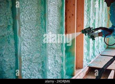 Baumeister isolierenden Holzrahmen Haus. Nahaufnahme eines Arbeiters, der Polyurethan-Schaum in der zukünftigen Hütte mit Plural Component Gun sprüht. Bau- und Isolierkonzept. Stockfoto