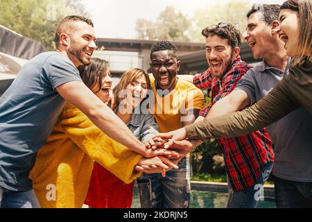 Fröhliche multiethnische Teamarbeit junger Menschen, die Spaß daran haben, die Hände zu verbinden - multirassische Freunde, die fünf zusammen haben - Vereinigung, Vielfalt, Integration Stockfoto