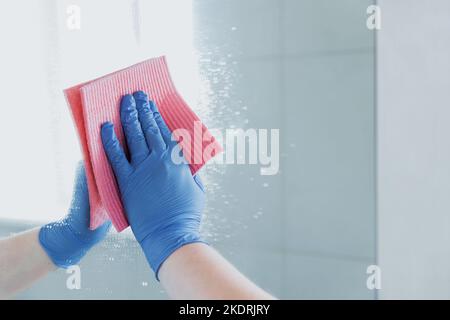 Beschnittene Ansicht der Haushälterin Frau Hand in blauen Gummihandschuh Polieren, Reinigung, Wischen Spiegel mit Tuch Lappen, Sprühen Reiniger Flüssigkeit während der Reinigung Bad zu Hause. Housekeeping, Reinigungsservice Stockfoto