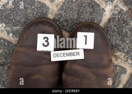 Dezember 31 geschrieben auf Holzwürfel liegt auf Winterstiefel auf einer Steinstraße auf der Straße im Winter, Happy New Year, Kalender und Zeit, Tapete Stockfoto