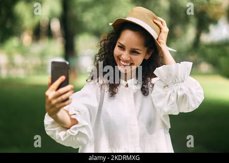 Junge schöne Mädchen in einem Hut macht ein Selfie auf ihrem Handy im Park Stockfoto