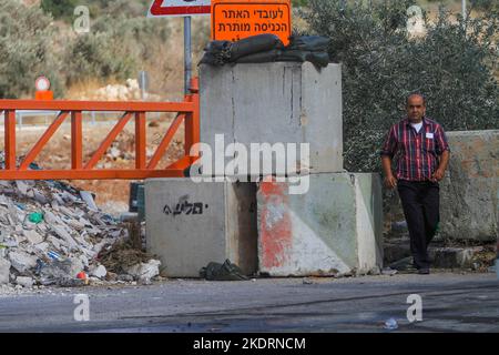 Qalqilya, Palästina. 8.. November 2022. Ein Palästinenser geht am Eingang des Dorfes Azzun vorbei, nachdem die israelische Armee es mit Erdhügeln und eisernen Toren blockiert hatte. Die israelische Armee schloss das Tor des Dorfes Azzun, östlich der Stadt Kalqilya im Westjordanland, nachdem palästinensische Jugendliche Steine auf die Fahrzeuge jüdischer Siedler geworfen hatten. Die israelische Armee teilte mit, dass ein israelischer Siedler aus der Siedlung Kedumim infolge seiner Wunden getötet wurde, die er erlitten hatte, nachdem er von einem Palästinenser erstochen wurde. Stockfoto