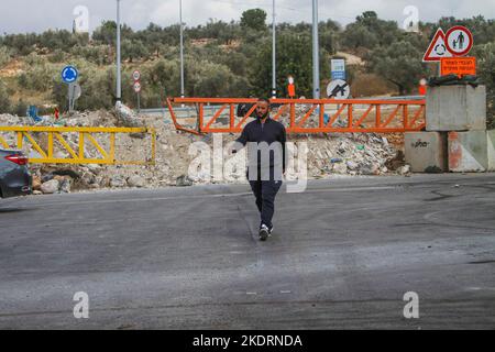 Qalqilya, Palästina. 8.. November 2022. Ein Palästinenser geht am Eingang des Dorfes Azzun vorbei, nachdem die israelische Armee es mit Erdhügeln und eisernen Toren blockiert hatte. Die israelische Armee schloss das Tor des Dorfes Azzun, östlich der Stadt Kalqilya im Westjordanland, nachdem palästinensische Jugendliche Steine auf die Fahrzeuge jüdischer Siedler geworfen hatten. Die israelische Armee teilte mit, dass ein israelischer Siedler aus der Siedlung Kedumim infolge seiner Wunden getötet wurde, die er erlitten hatte, nachdem er von einem Palästinenser erstochen wurde. Stockfoto