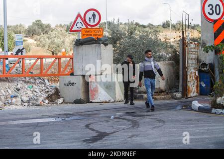 Qalqilya, Palästina. 8.. November 2022. Palästinensische Männer gehen am Eingang des Dorfes Azzun vorbei, nachdem die israelische Armee es mit Erdhügeln und eisernen Toren blockiert hatte. Die israelische Armee schloss das Tor des Dorfes Azzun, östlich der Stadt Kalqilya im Westjordanland, nachdem palästinensische Jugendliche Steine auf die Fahrzeuge jüdischer Siedler geworfen hatten. Die israelische Armee teilte mit, dass ein israelischer Siedler aus der Siedlung Kedumim infolge seiner Wunden getötet wurde, die er erlitten hatte, nachdem er von einem Palästinenser erstochen wurde. Stockfoto