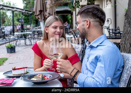 Glückliches romantisches Paar, das lacht und eine gute Zeit beim Abendessen oder Mittagessen in einem wunderschönen Restaurant im Freien hat. Stockfoto