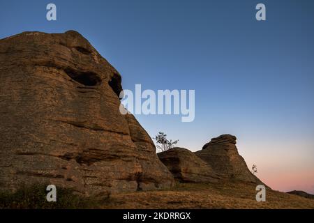 Heilige Felsen, Berge in der Form eines Kopfes, der von der untergehenden Sonne beleuchtet wird. Rock Bergklippe über Sonnenuntergang Himmel Hintergrund Ein Ort der Macht. Ein Ort Stockfoto