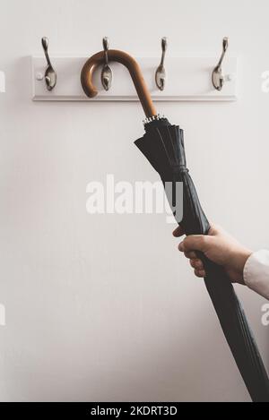 Die Hand eines Mannes hängt einen Regenschirm auf oder vom Regal Stockfoto