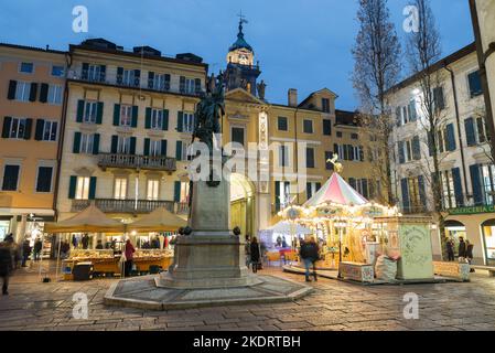 Weihnachtsmarkt in der Abenddämmerung. Varese, Italien. Stadtstraße mit weihnachtsbeleuchtung. Historisches Zentrum von Varese mit Ständen und einem Karussell Stockfoto